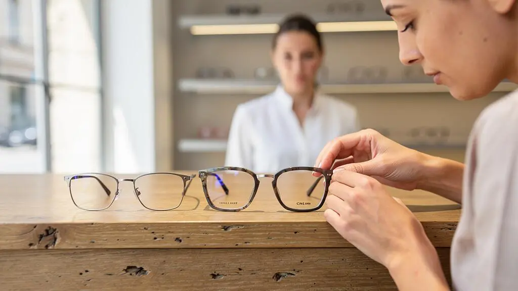 Un opticien présente plusieurs montures de lunettes de matières différentes à une cliente en boutique.